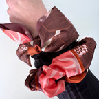 Three patterned scrunchies on a wrist against a light background