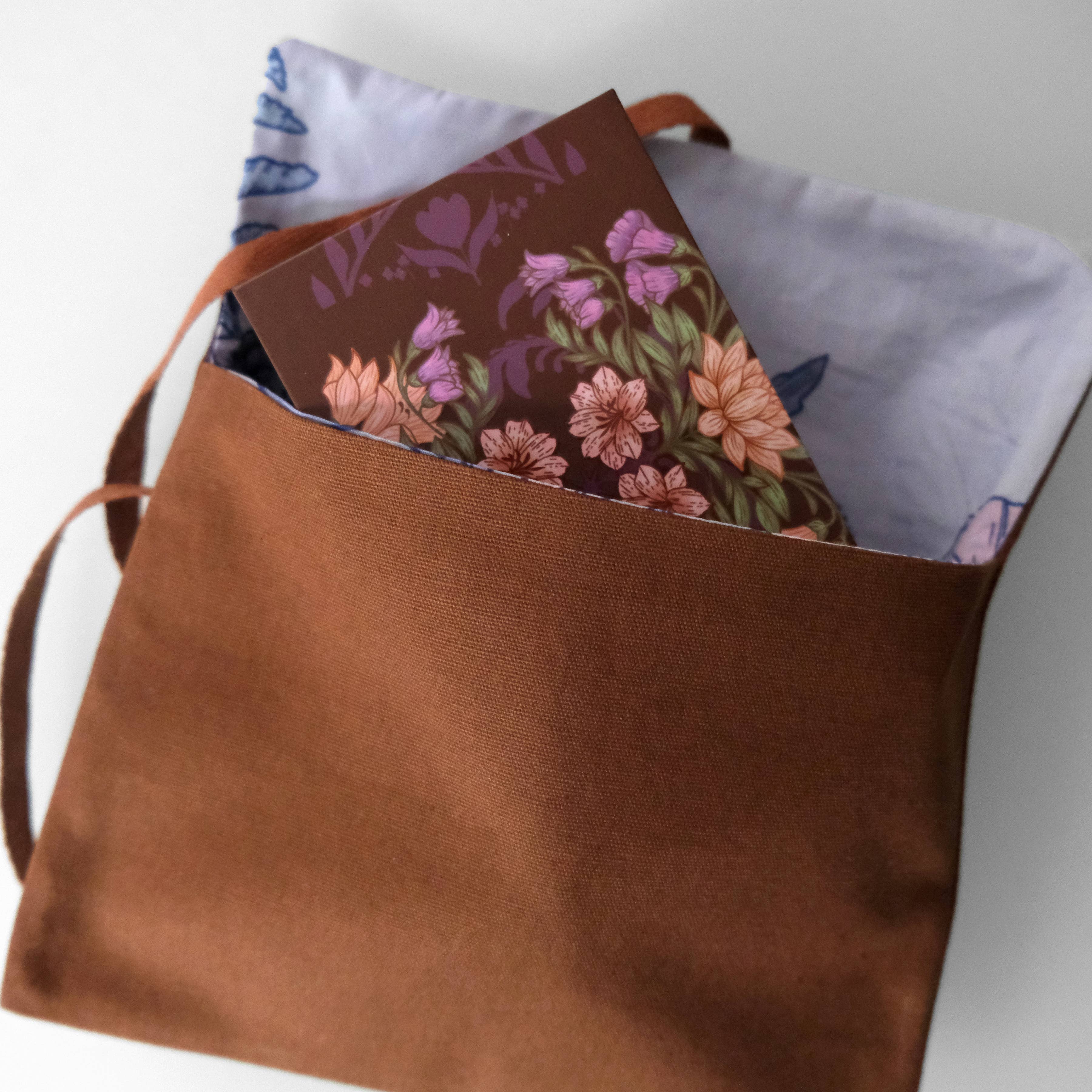 Brown leather bag with a floral notebook and fabric lining on a white background