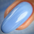 A close-up of a glossy light blue nail tip with a soft shimmer, shown resting against natural skin.