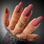 Hand with long, dark pink nails and gold rings on a blurred background