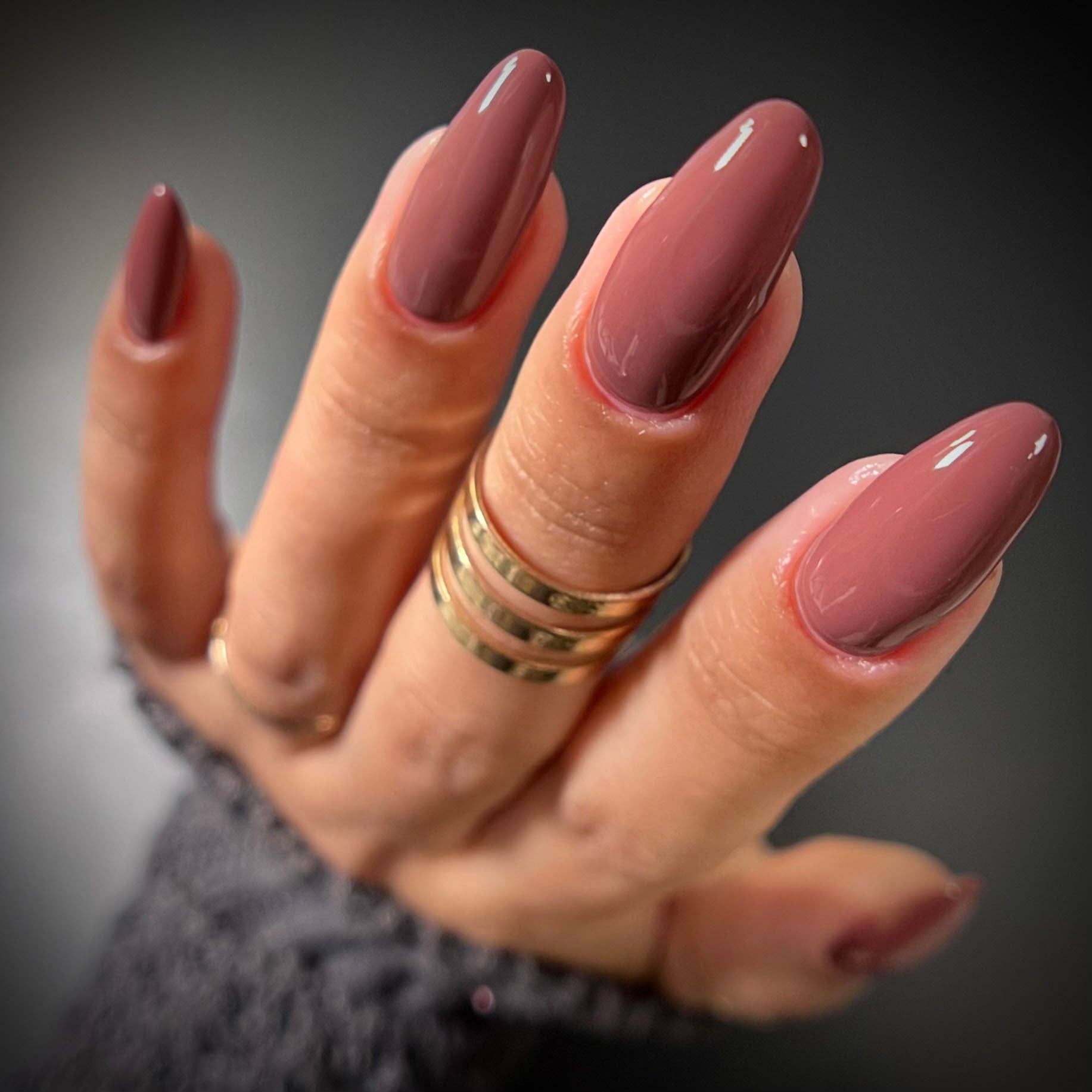 Hand with long, dark pink nails and gold rings on a blurred background