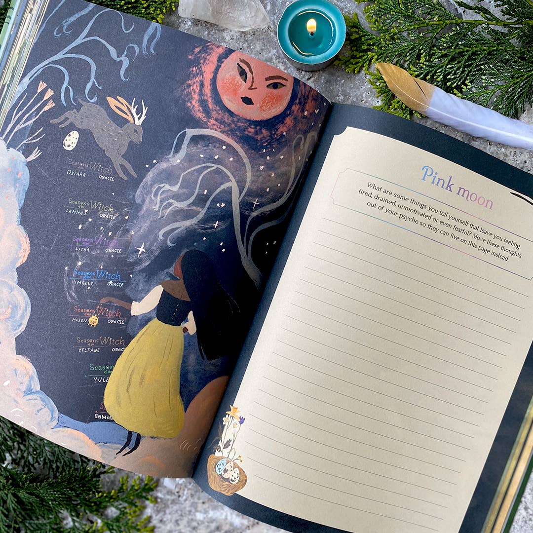 Open notebook with celestial design on cover and lined pages, surrounded by greenery and a candle.
