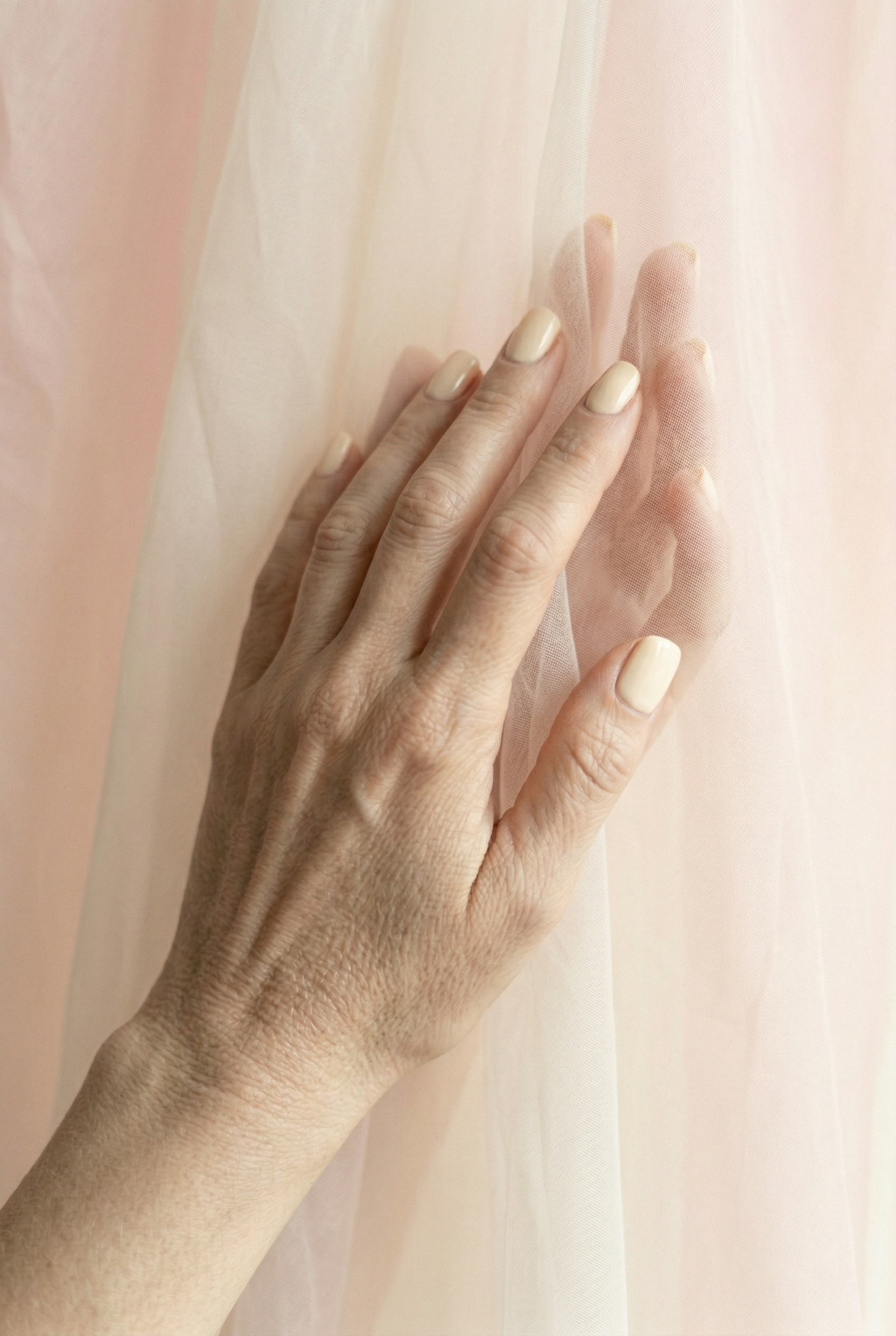 Close-up of two hands with light nail polish against a soft pink background