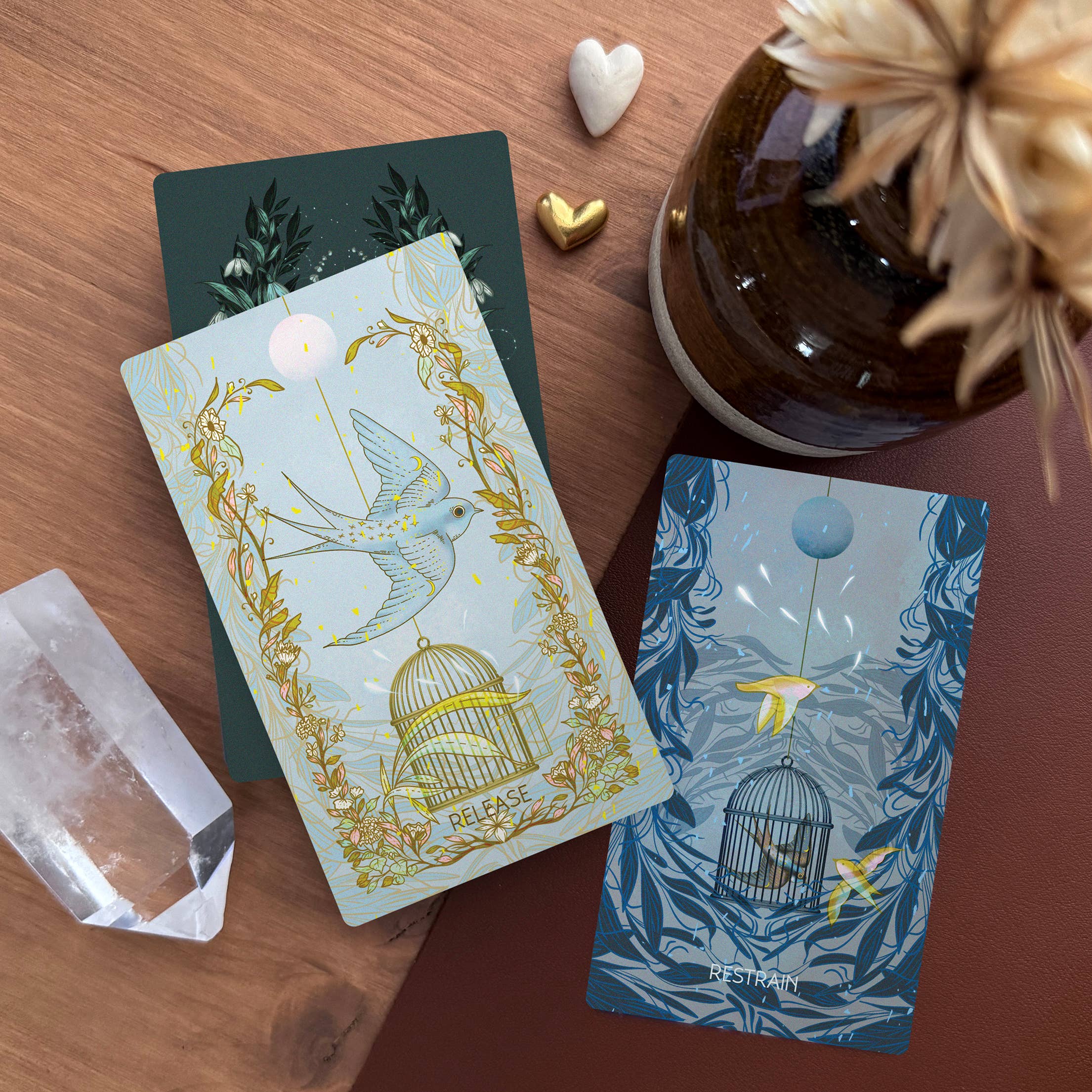 Two tarot cards with decorative designs on a wooden surface with a vase and crystal.