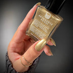 Hand holding a gold nail polish bottle labeled 'Abundance Boost' against a dark background