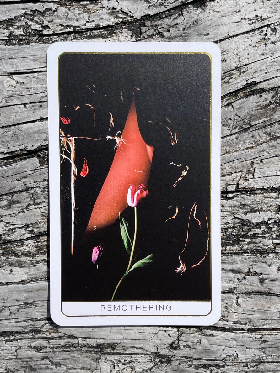 Tarot card titled 'Remothering' with a red heart and flowers on a dark background, placed on a wooden surface.