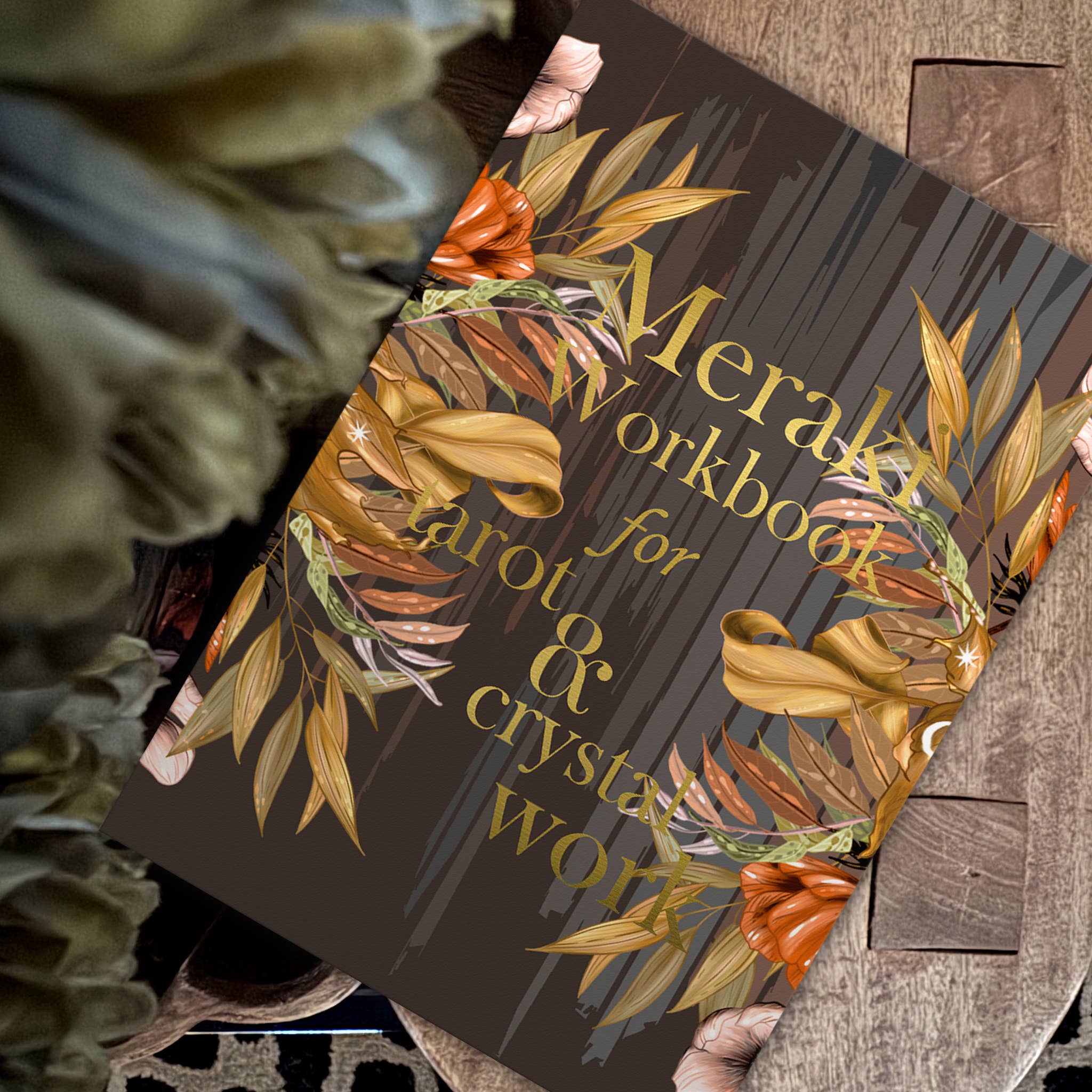 Workbook titled 'Meraki Workbook for Tarot & Crystal Work' with leaf design on a wooden surface.