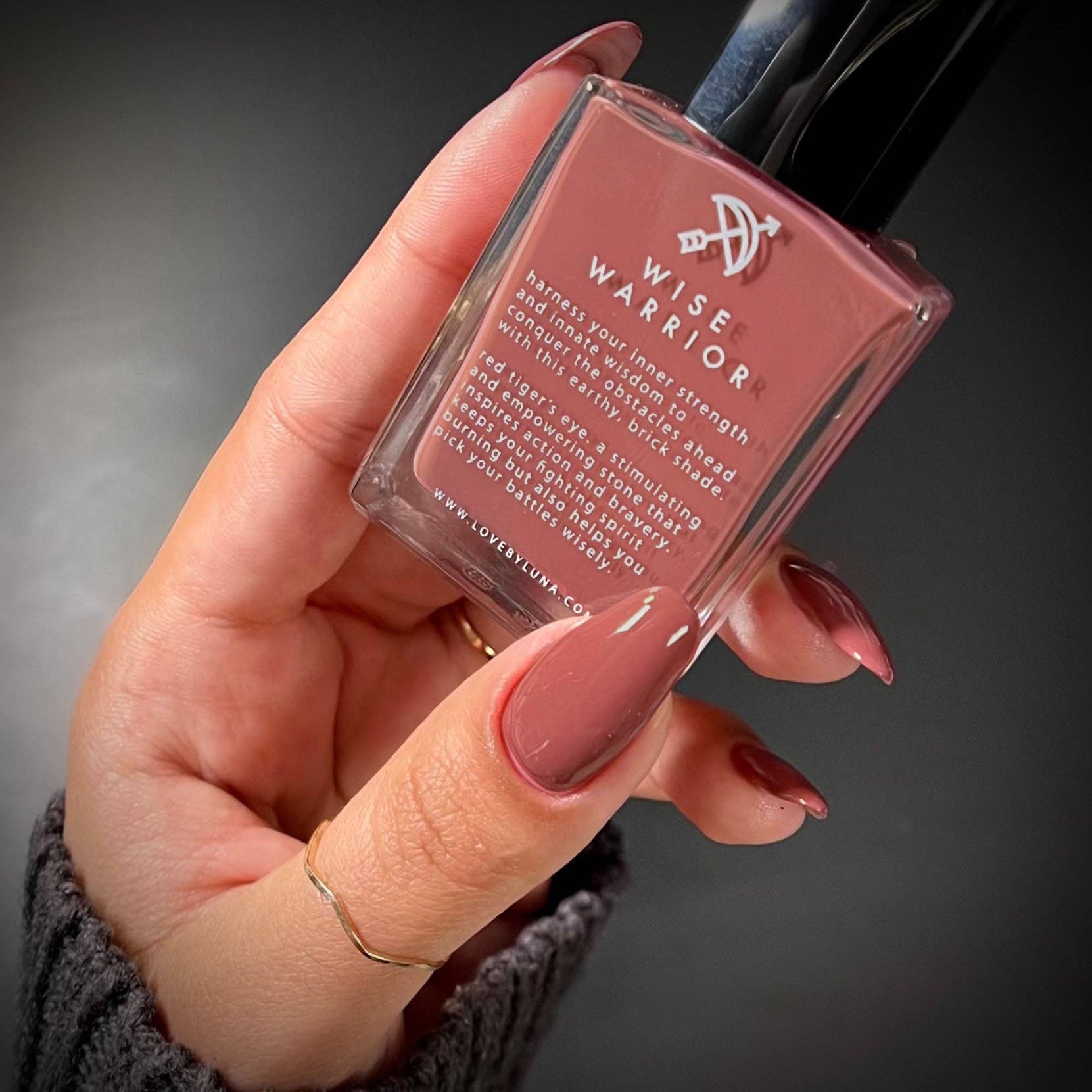 Hand holding a bottle of Wise Warrior nail polish with a dark background