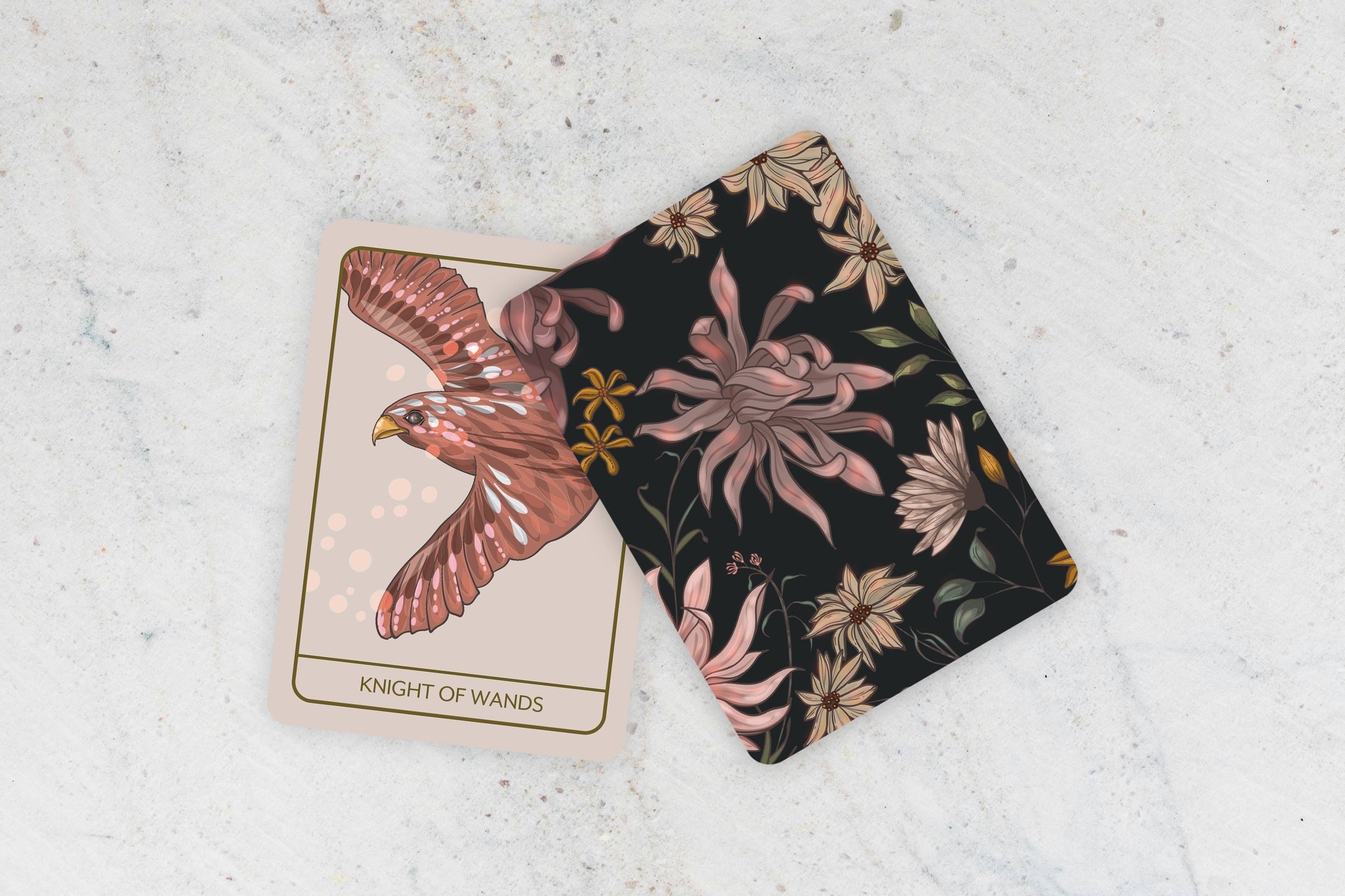 Two tarot cards on a textured surface, one with an eagle design and the other with floral patterns.