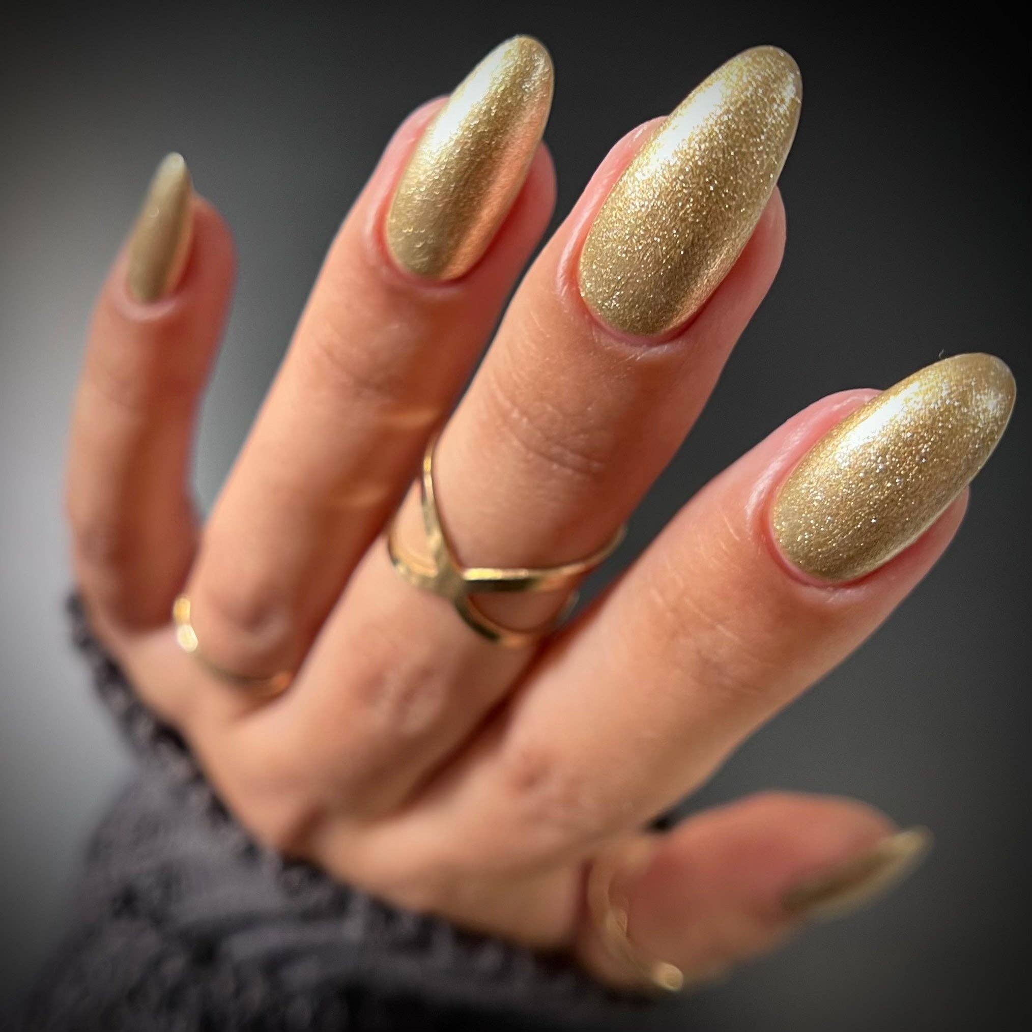Hand with gold glittery nail polish on a dark background