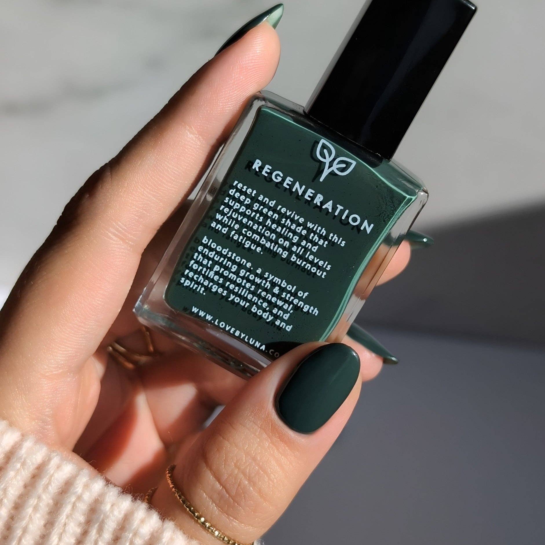 Hand holding a green nail polish bottle labeled 'Regeneration' against a neutral background