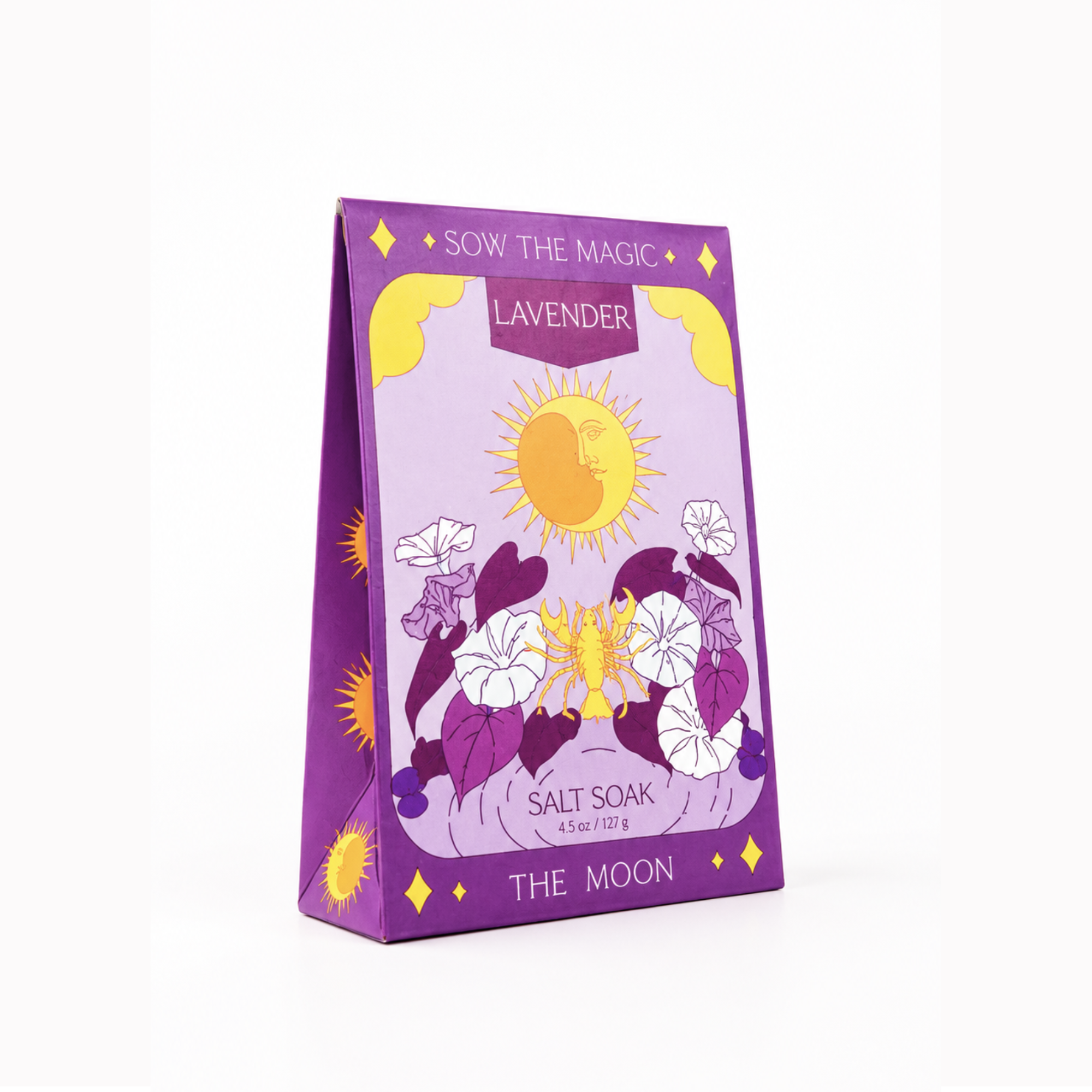 A purple triangular box of SOW THE MAGIC Lavender Salt Soak, featuring a whimsical illustration of a yellow sun, white flowers, and the text 'THE MOON' on a clean white background.