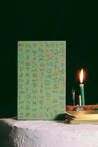 Green notebook with symbols on a white surface with a candle in the background