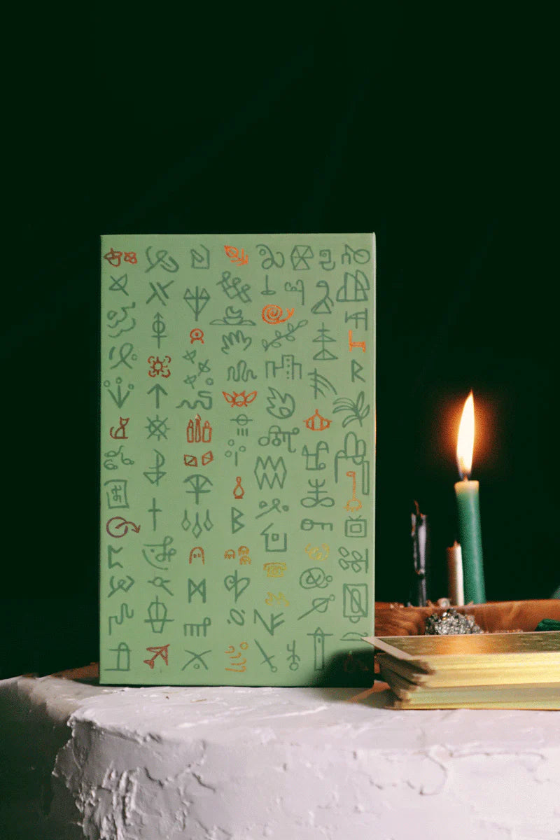 Green notebook with symbols on a white surface with a candle in the background