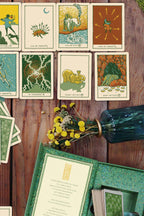 Collection of tarot cards on a wooden surface with a vase and flowers.