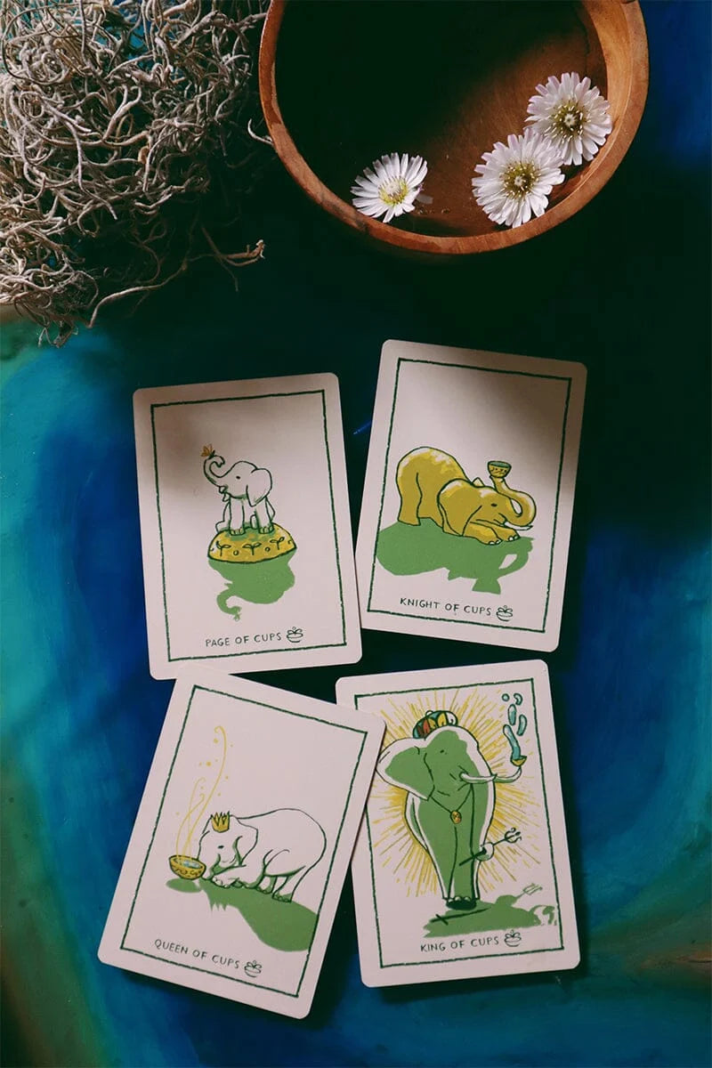 Four tarot cards with animal illustrations on a blue surface with a bowl of flowers.