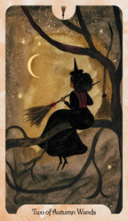 A tarot card illustration titled 'Two of Autumn Wands' showing a witch in a black dress and hat riding a broomstick on a tree branch under a crescent moon and stars.
