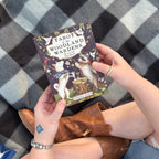 Person holding a tarot card deck titled 'Tarot of the Woodland Wardens' against a checkered fabric background.