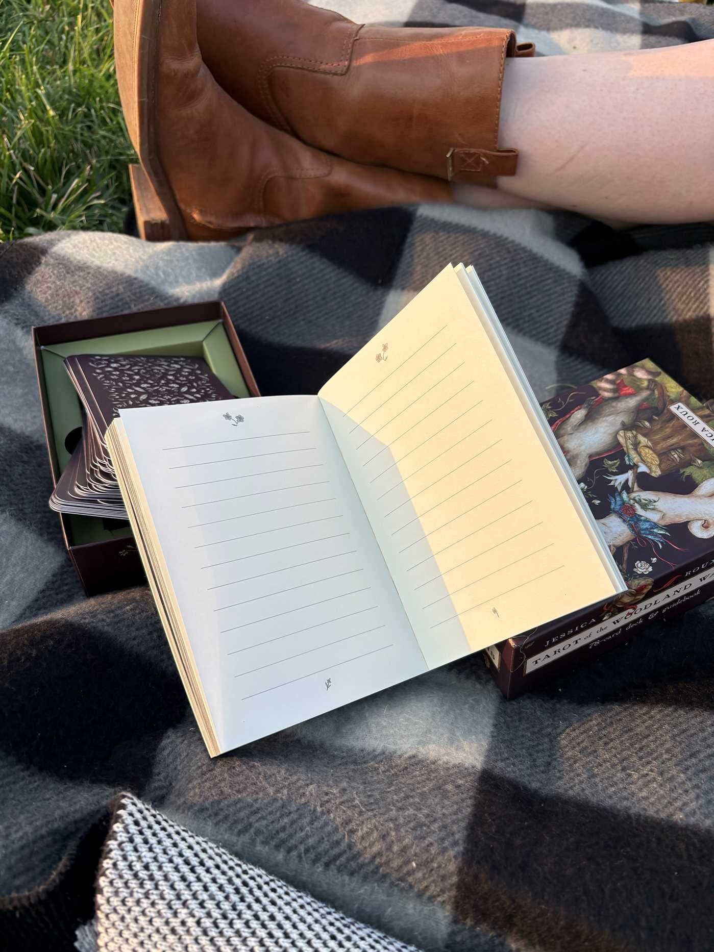 Open notebook on a blanket with a person's foot in a brown boot in the background.